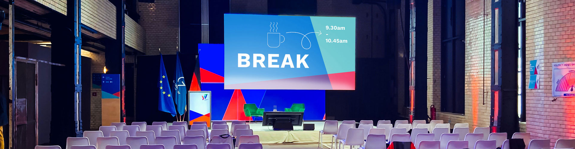Y7 Youth Summit, G7 Jugendgipfel, Berlin, Key Visual Ausarbeitung, Stage Design, Rednerpult dahinter die Flagge von Deutschland, der EU und der G7 Staaten, Rede, Bühne, Stage, Mittagspause, leere Stühle, Design Simpelplus Agentur für Event Design, Eventdesign