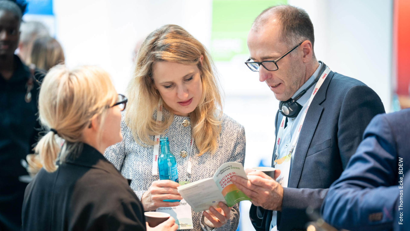 Teilnehmende beim Treffpunkt Netze 2025 im Gespräch mit Programmflyer und Event Branding im Hintergrund.